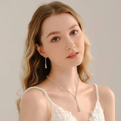 A young woman with wavy blonde hair and fair skin, wearing a white lace dress and silver jewelry, looks serenely at the camera.