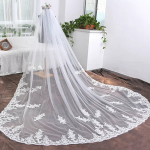 A long bridal veil with intricate lace detailing spread out on a brown floor, contrasting against a bright, modern room background.