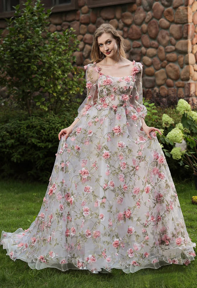 A woman in a Romantic Square Neckline with 3D Flowers Bridal Gown With Detachable Sleeves by Bergamot Bridal is posing outside an elegant bridal shop in London.