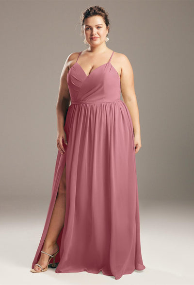 A woman in a Wilfreda - Chiffon Bridesmaid Dress - Off The Rack by Bergamot Bridal posing confidently on a gray background.