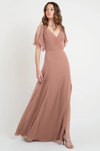 Woman in a beautiful, dusky pink Hayes - Bridesmaid Dress by Jenny Yoo with flutter sleeves, sample size 24, standing against a plain background from Bergamot Bridal.