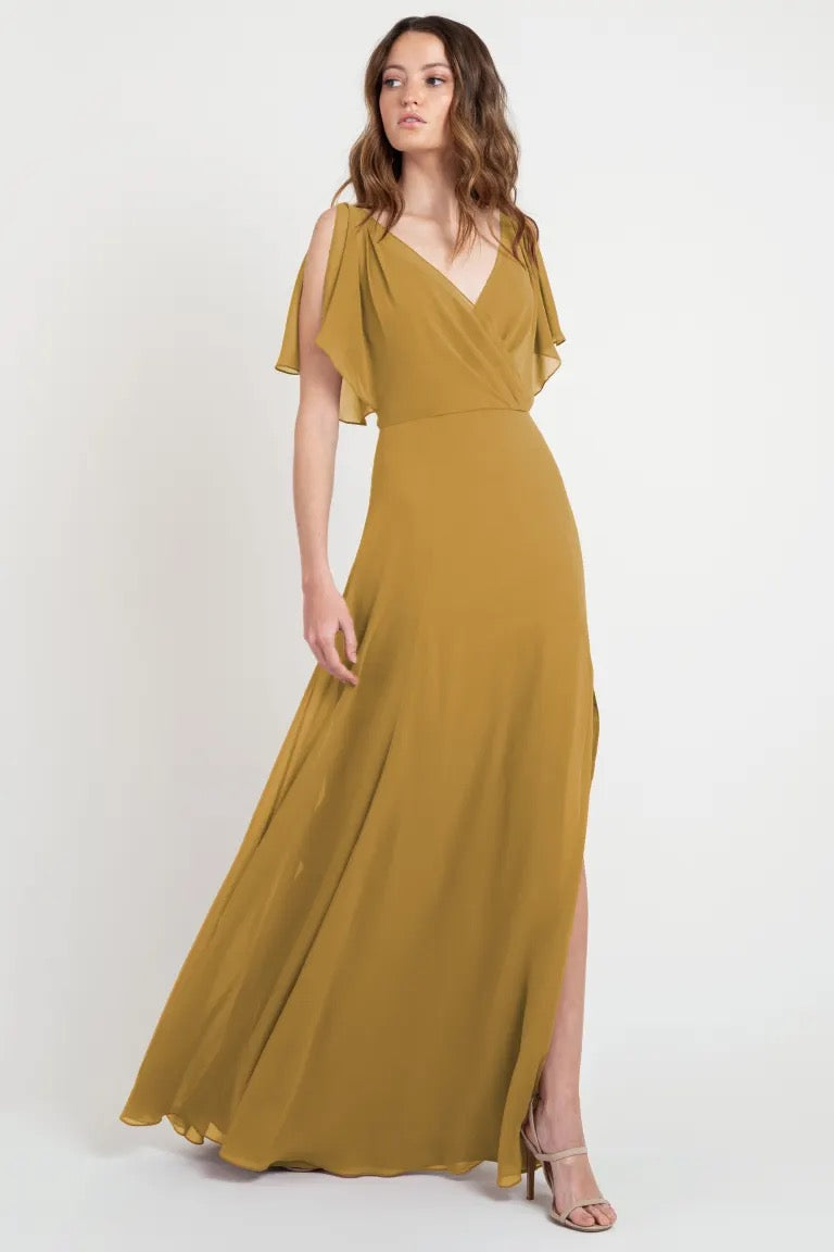 Woman posing in an elegant mustard-colored Hayes - Bridesmaid Dress by Jenny Yoo with flutter sleeves from Bergamot Bridal.