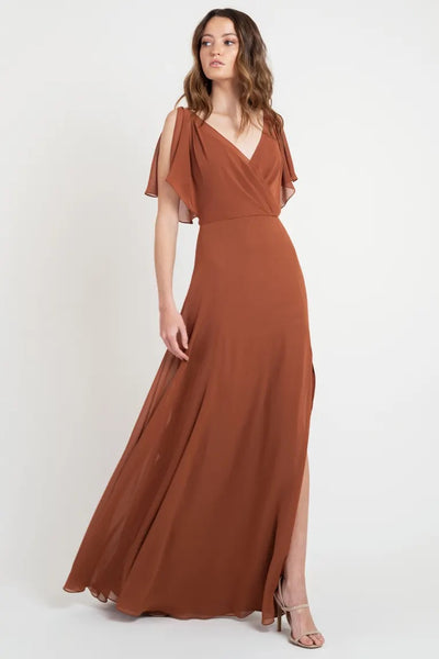 Woman posing in a beautiful, flowing rust-colored Hayes - Bridesmaid Dress by Jenny Yoo with short flutter sleeves, size 24 from Bergamot Bridal.