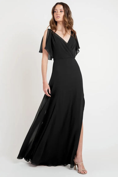 Woman modeling a size 24 black flowy evening goddess dress with flutter sleeves, the Hayes Bridesmaid Dress by Jenny Yoo from Bergamot Bridal.
