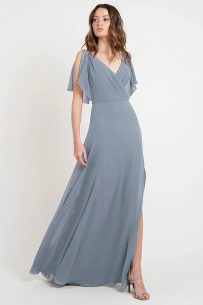 Woman posing in a beautiful dress, a flowing grey evening gown with flutter sleeves and a thigh-high slit, size 24 - Hayes Bridesmaid Dress by Jenny Yoo from Bergamot Bridal.