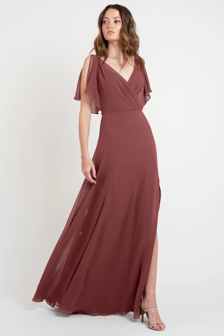 Woman modeling an elegant, dusty rose evening gown with flutter sleeves and a v-neckline, available in sample size 24. Product: Hayes - Bridesmaid Dress by Jenny Yoo from Bergamot Bridal.