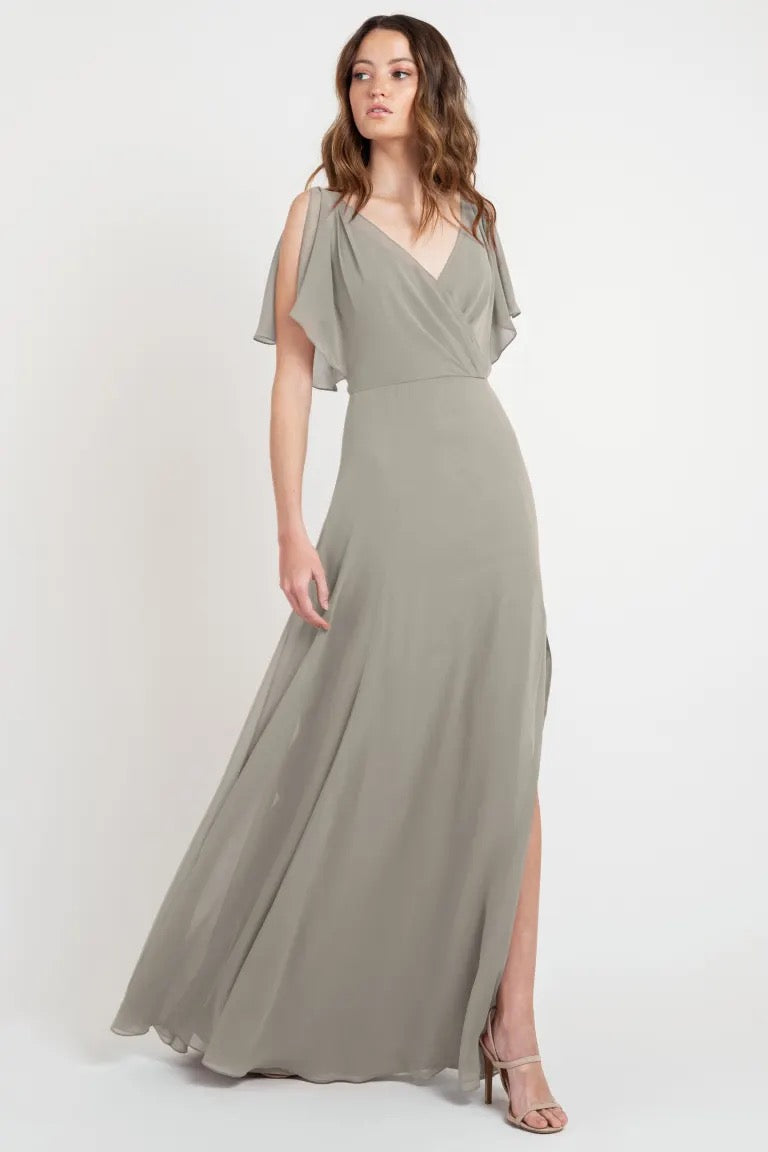 A woman in an elegant, size 24 Hayes - Bridesmaid Dress by Jenny Yoo with flutter sleeves stands against a white background from Bergamot Bridal.