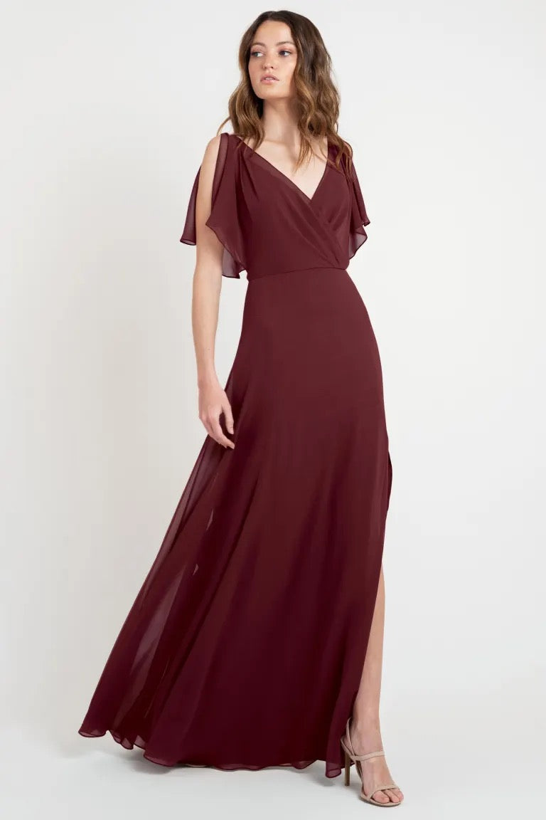Woman posing in a beautiful maroon evening gown with flutter sleeves, sample size 24, Hayes - Bridesmaid Dress by Jenny Yoo from Bergamot Bridal.