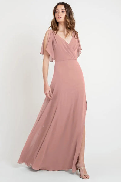 A woman in a beautiful dress, a flowing pink evening gown with flutter sleeves and a v-neckline, the Hayes - Bridesmaid Dress by Jenny Yoo at Bergamot Bridal.