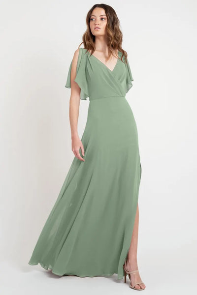 Woman in an elegant Hayes - Bridesmaid Dress by Jenny Yoo with flutter sleeves and a thigh-high slit posing for the camera, available at Bergamot Bridal.