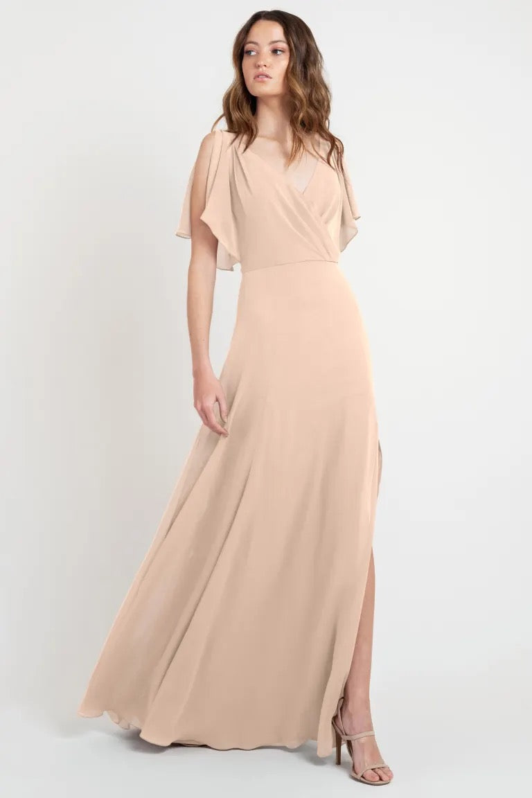 A woman models a beautiful, flowing beige maxi dress with flutter sleeves, offered in store sample size 24. This is the Hayes bridesmaid dress by Jenny Yoo from Bergamot Bridal.