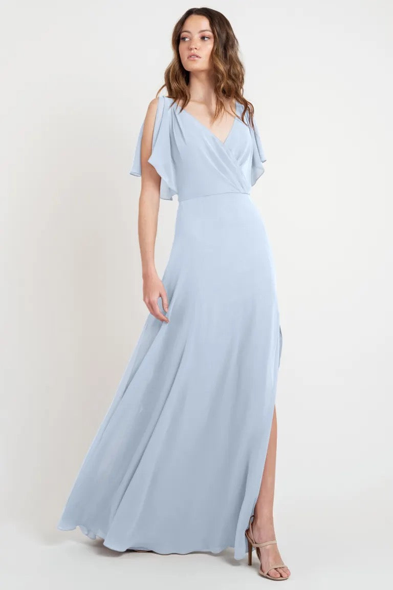 Woman in a beautiful, light blue, flowy evening gown with flutter sleeves and a side slit - Hayes Bridesmaid Dress by Jenny Yoo at Bergamot Bridal.