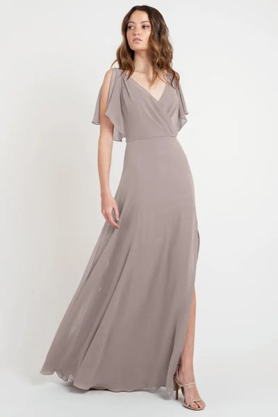 A woman modeling a beautiful dress, a taupe evening gown with a v-neckline and flutter sleeves, in store sample size 24 of the Hayes - Bridesmaid Dress by Jenny Yoo from Bergamot Bridal.