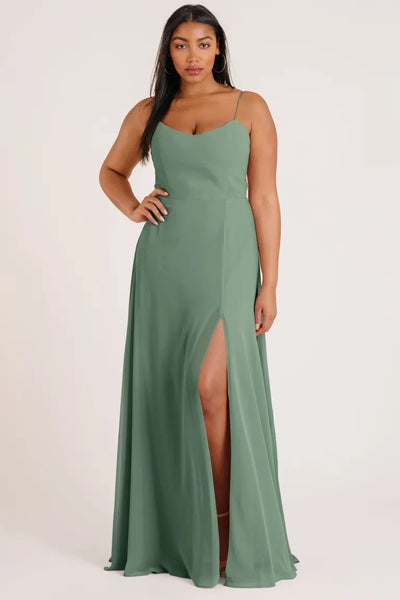 Woman posing in an elegant green Kiara - Bridesmaid Dress by Jenny Yoo with spaghetti straps and a thigh-high slit from Bergamot Bridal.