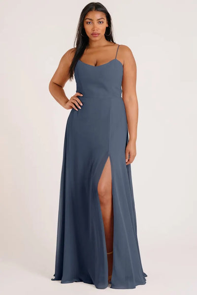 A woman models the luxe chiffon Kiara bridesmaid dress by Jenny Yoo, featuring a slate blue A-line skirt with a high leg slit from Bergamot Bridal.