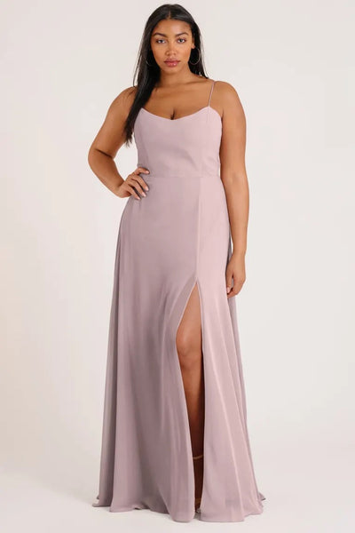 A woman wearing a luxe chiffon Kiara - Bridesmaid Dress by Jenny Yoo, designed as a sleeveless mauve evening gown with a thigh-high slit and scoop neck from Bergamot Bridal.