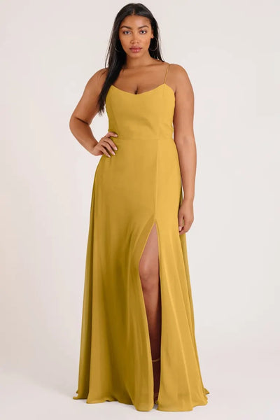 A woman posing in a luxe chiffon, mustard yellow Kiara bridesmaid dress by Jenny Yoo with a high side slit from Bergamot Bridal.