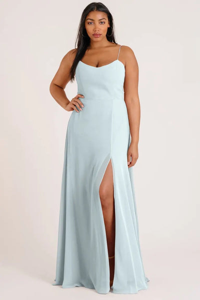 A woman standing and posing in a light blue Kiara Bridesmaid Dress by Jenny Yoo with a high slit from Bergamot Bridal.