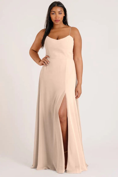 A woman posing in an elegant beige Kiara - Bridesmaid Dress by Jenny Yoo with a thigh-high slit from Bergamot Bridal.