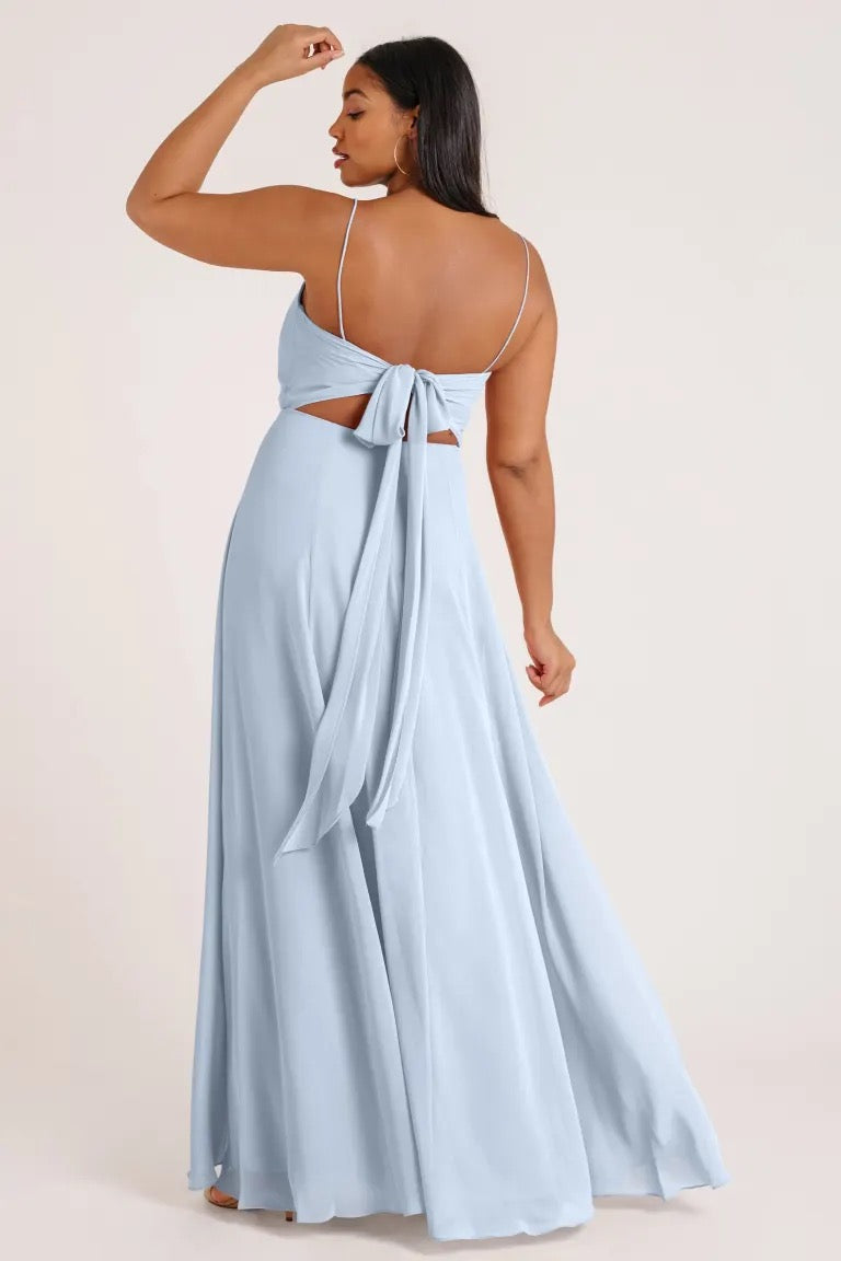 Woman in a luxe chiffon Kiara - Bridesmaid Dress by Jenny Yoo with an open back and bow detail standing with her hand on her head from Bergamot Bridal.