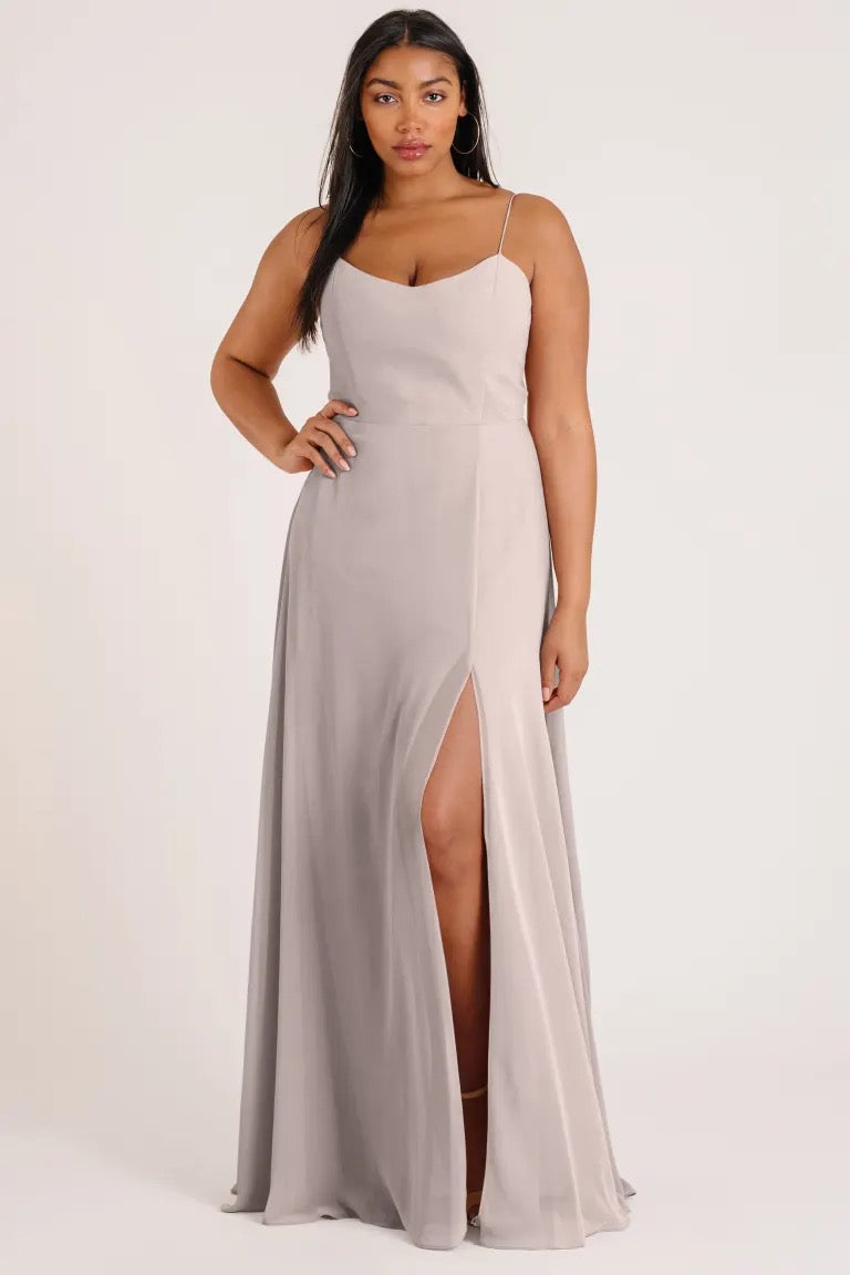 A woman posing in a luxe chiffon Bridesmaid Dress by Jenny Yoo with a thigh-high slit and an A-line skirt from Bergamot Bridal.