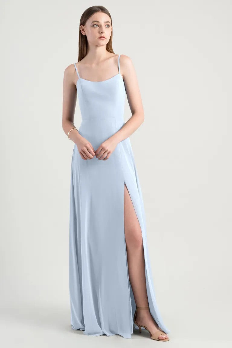 A woman in a luxe chiffon Kiara Bridesmaid Dress by Jenny Yoo with a high slit and an A-line skirt, standing against a neutral background from Bergamot Bridal.