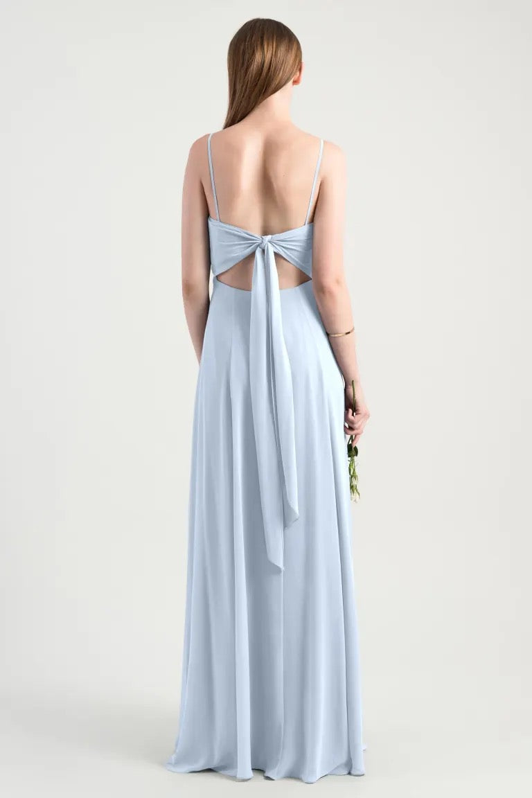 Woman in a luxe chiffon Kiara - Bridesmaid Dress by Jenny Yoo with an A-line skirt and a bow, holding flowers from Bergamot Bridal.