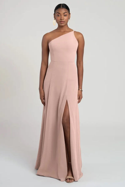 A woman in an elegant one-shoulder blush pink chiffon bridesmaid dress with a high slit from the Kora by Jenny Yoo Bridesmaid Dress collection at Bergamot Bridal.