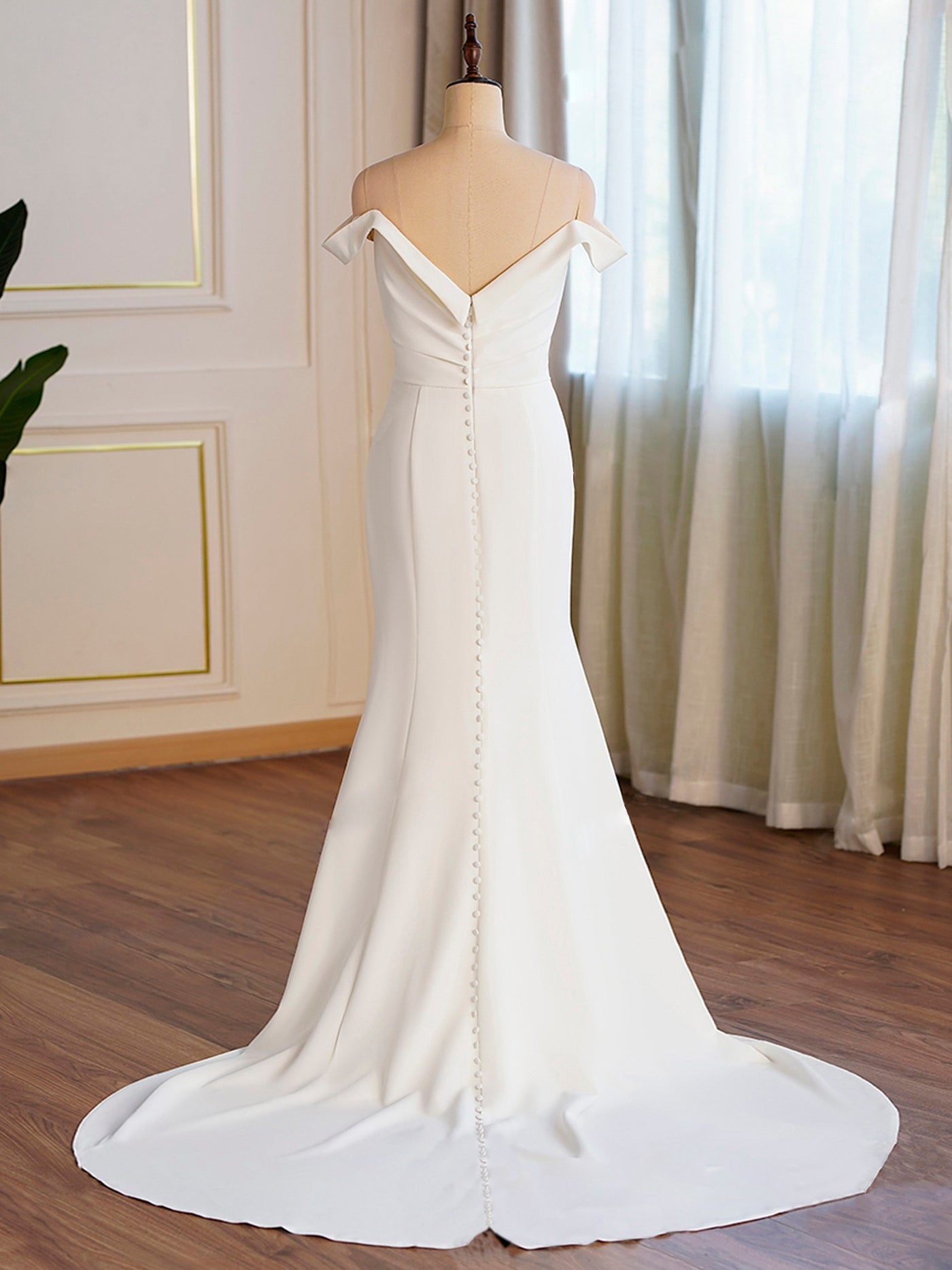 Elegant Bergamot Bridal white wedding dress with an off-shoulder design and a train, displayed on a mannequin in one of the bridal shops in London, Ontario, adorned with curtains.