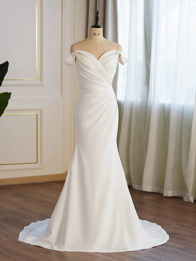 An elegant Bergamot Bridal Crepe Off-the-shoulder Pleated Fit And Flare Bridal Gown displayed on a mannequin in a room with curtains and a wooden floor.