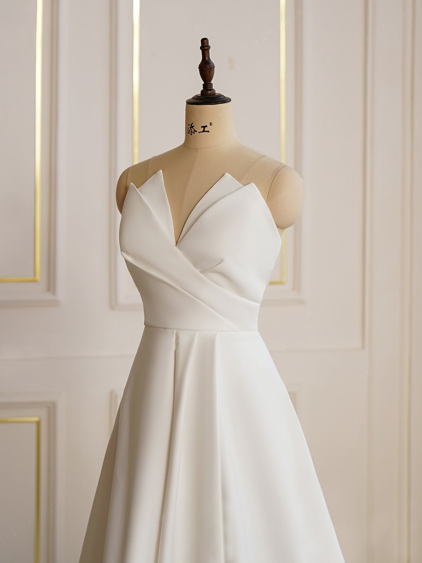 A Bergamot Bridal Modern Satin A-line Wedding Dress with Slit is displayed on a mannequin dummy in a bridal shop.