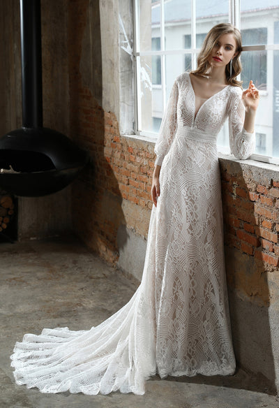 A woman in a Bergamot Bridal Plunging V-neck Lace Long Sleeve Bohemian Wedding Gown leaning against a window.