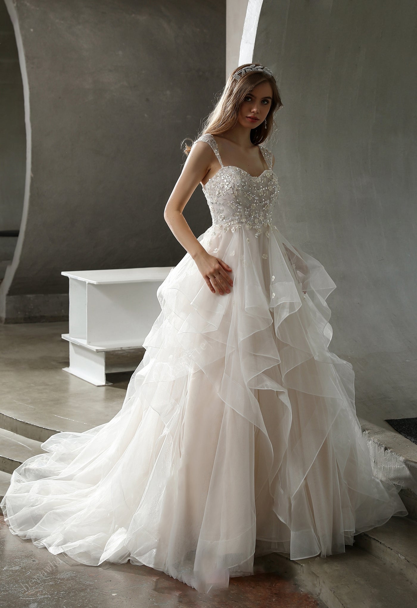 A woman in Bergamot Bridal is standing in a room wearing the Beaded Ruffled Ball Gown With Cap Sleeves.
