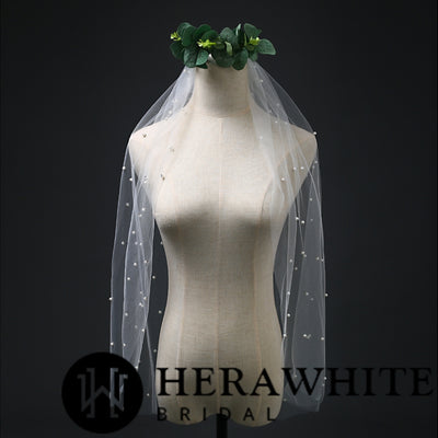 A mannequin displaying a wedding dress with a Ivory Pearl Beaded Bridal Veil by Bergamot Bridal, against a dark background.