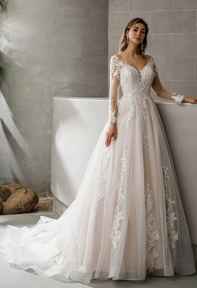 A bride in an "Illusion Tattoo Lace Sleeve V-Neck A-Line Ballgown Bridal Gown" by Bergamot Bridal leaning against a wall.