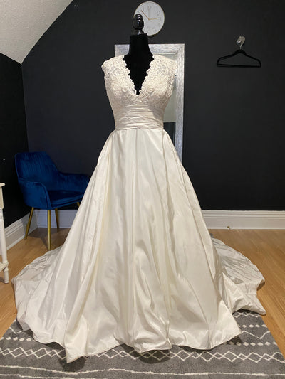 An elegant Watters "Escalante" Bridal Gown - Off The Rack with lace bodice on a mannequin in a room with black walls and a blue chair.