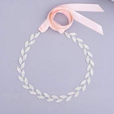 A delicate bridal headpiece with a leaf pattern made from white crystals, featuring a long, light pink ribbon with multiple color options, displayed on a gray background.
