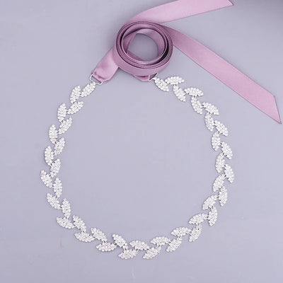 A Silver leaf crystal bridal belt sash with a soft pink crystals ribbon on a light gray background.