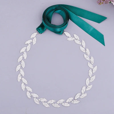 A Bergamot Bridal silver leaf crystal bridal belt sash with a green crystals ribbon on a lavender background.