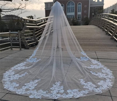 A long Bergamot Bridal lace appliqued cathedral veil spread out on a wooden bridge, with a building in the background, near one of the bridal shops in London, Ontario.