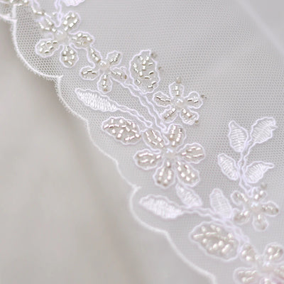 Close-up of delicate Bergamot Bridal embroidered lace edged fingertip length bridal veil featuring intricate floral embroidery with shimmering thread accents, perfect for wedding dresses in London, Ontario.