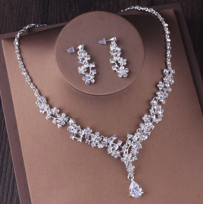 Bergamot Bridal silver crystal bridal jewelry set, including necklace, earrings & tiara, displayed on a brown surface.
