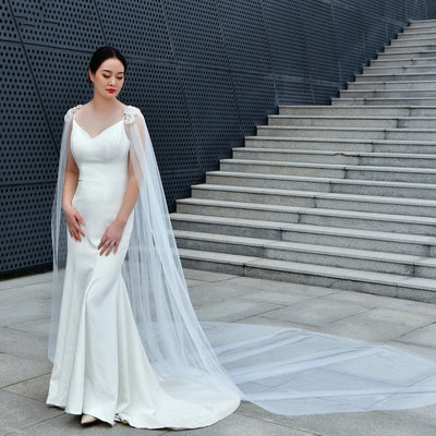 A bride in a white gown and veil from Bergamot Bridal, one of the renowned bridal shops in London stands in front of a stairway with a geometric patterned wall.