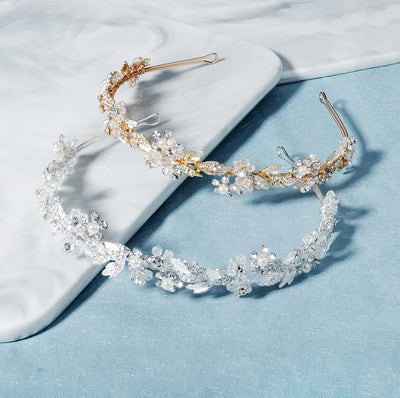 Two Gold & Crystal Floral Hairbands by Bergamot Bridal on a marble table at bridal shops.