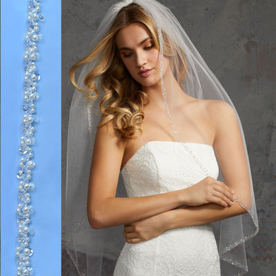 A bride in a strapless lace gown and Bergamot Bridal wedding veil with pearl & crystal beaded edging, purchased from one of the bridal shops in London, Ontario, looking downward thoughtfully, with a decorative blue border to her left.