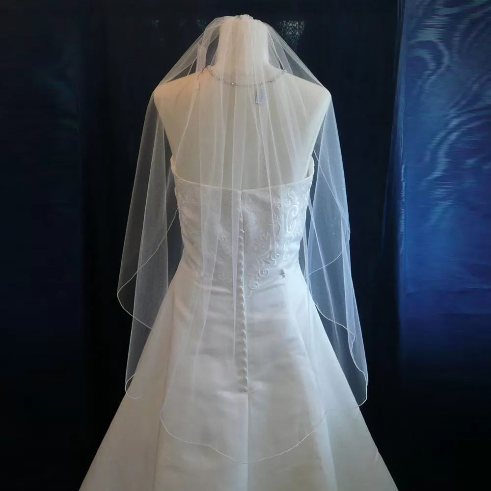 A back view of a strapless white wedding dress with an Ivory Single Tiered Bridal Veil by Bergamot Bridal, displayed on a mannequin against a dark background.