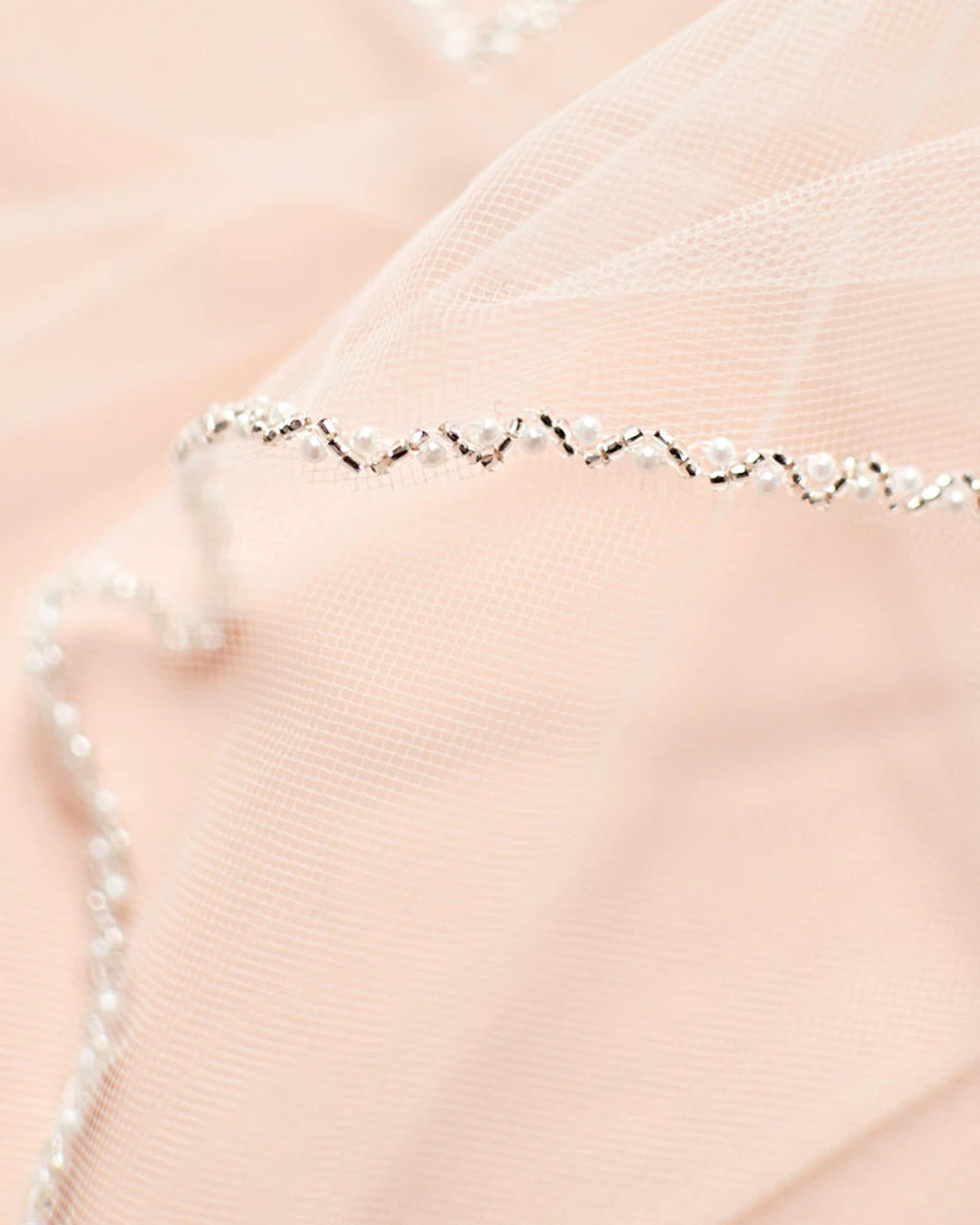 Close-up of a delicate Bergamot Bridal Crystal Organza Beaded Wedding Veil lying on a soft pink tulle fabric, perfect for bridal accessories, focusing on the intricate details of the chain.