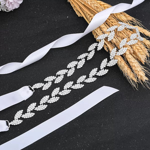 A decorative crystal and ribbon hair accessory displayed on a black background, next to a bundle of dried wheat.