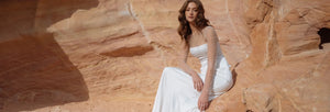 A woman in a white dress posing against a rocky desert backdrop.