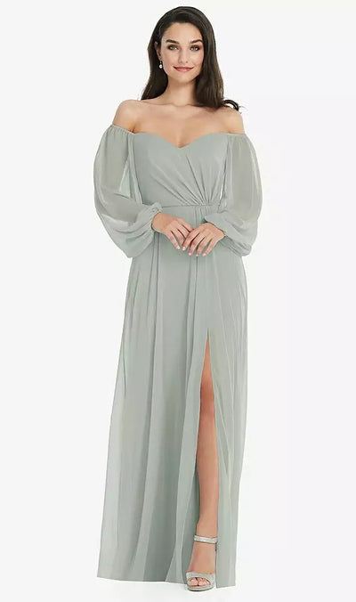 A person stands gracefully, smiling in a Bergamot Bridal off-the-shoulder puff sleeve maxi dress. The light gray Dessy Collection Style 3104 gown features sheer sleeves and a captivating front leg slit, perfect for bridesmaids.